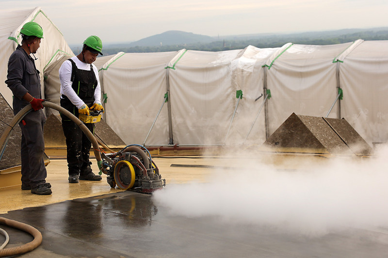 Zwei Arbeiter mit einem Wasserstrahlroboter bei der Behandlung der Gasometer-Dachfläche.