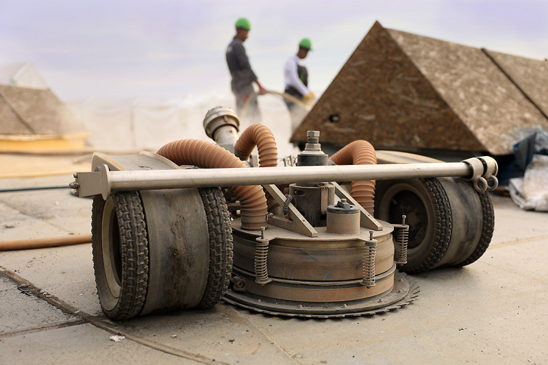Im Vodergrung ist ein Roboter zu sehen, im Hintergrund zwei Arbeiter auf dem Gasometerdach.