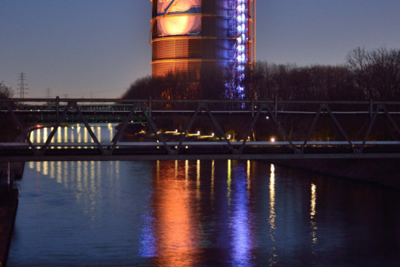 Der Gasometer am Abend mit großer Reklame für die Christo Ausstellung an der Fassade.