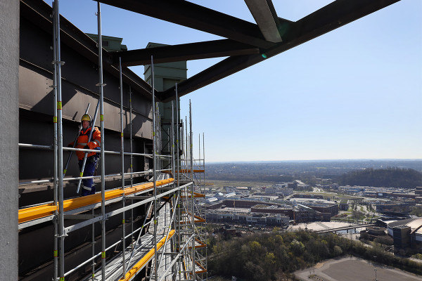 Ein Gerüstbauer stellt in luftiger Höhe das Fassadengerüst des Gasometers fertig.